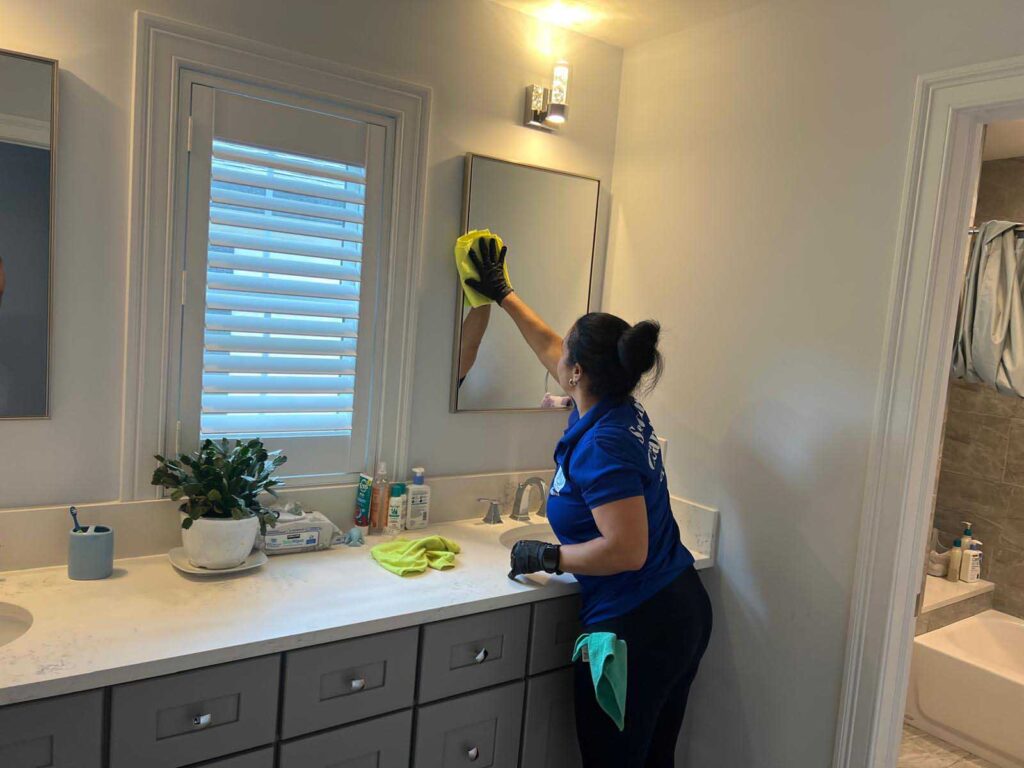Santana Cleaning Services professional wiping down a bathroom mirror and countertop in New Jersey.