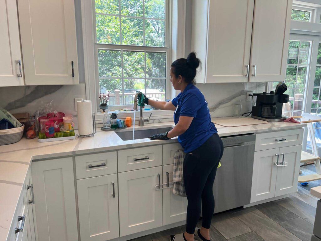 Professional cleaner from Santana Cleaning Services disinfecting a kitchen sink in a modern NJ home.