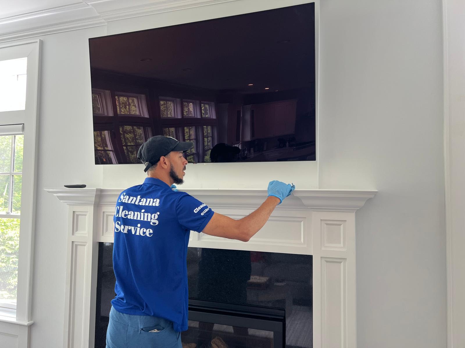 "Male professional from Santana Cleaning Services dusting TV and fireplace mantel in a New Jersey home"