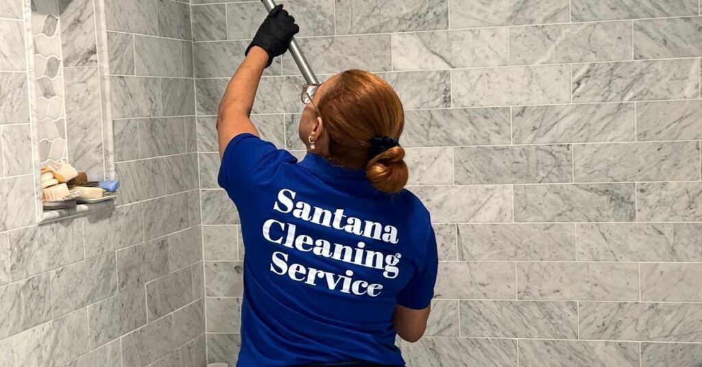 Person cleaning a tiled shower wall with a long scrub brush.
